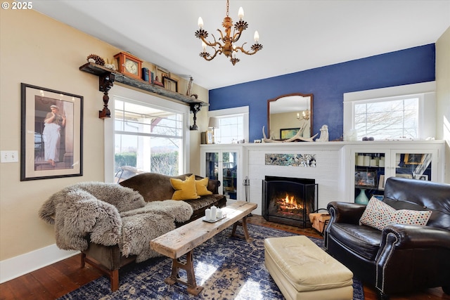 living room with baseboards, a brick fireplace, wood finished floors, and a notable chandelier