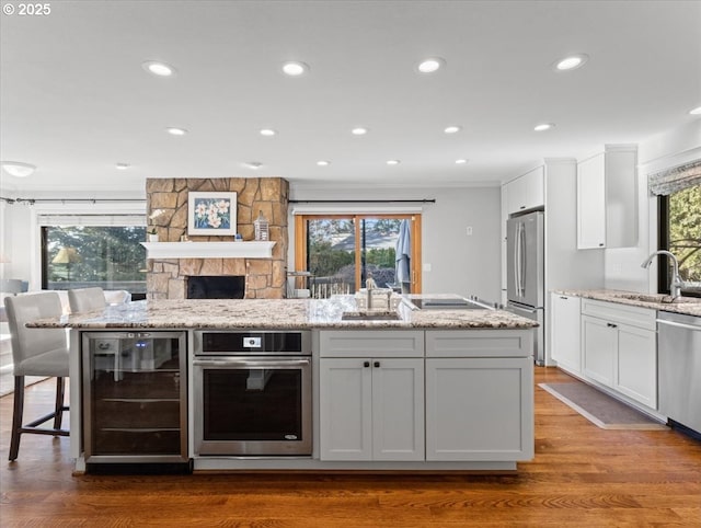 kitchen with wine cooler, stainless steel appliances, white cabinets, a sink, and light stone countertops