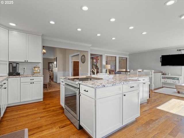 kitchen featuring a kitchen island with sink, white cabinetry, stainless steel range with electric cooktop, open floor plan, and ornamental molding