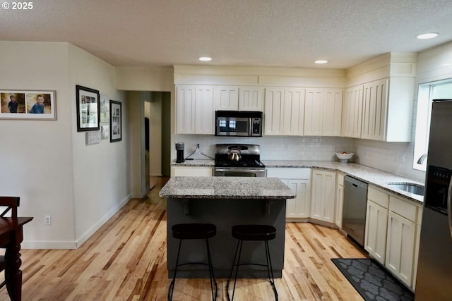 kitchen with light wood finished floors, stainless steel appliances, a textured ceiling, backsplash, and a kitchen island
