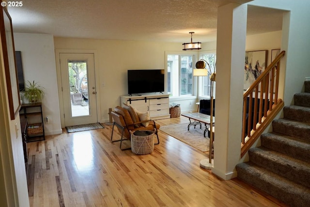 living room with a textured ceiling, stairway, light wood-style flooring, and baseboards