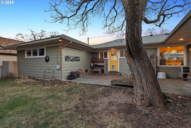 back house at dusk featuring a lawn and a patio area