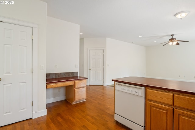 kitchen with built in study area, dark countertops, white dishwasher, dark wood-type flooring, and ceiling fan