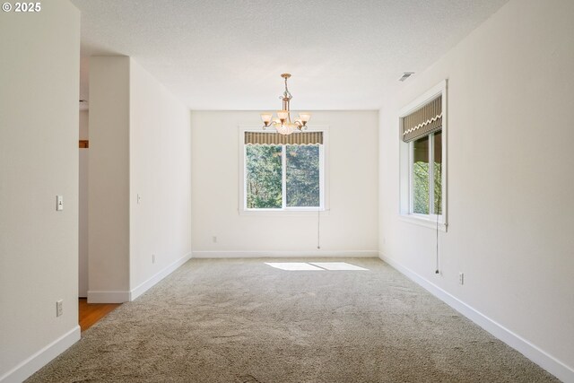 carpeted spare room with baseboards, a chandelier, and visible vents