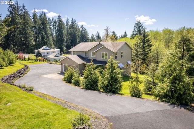 exterior space featuring an attached garage, driveway, a forest view, and a front yard