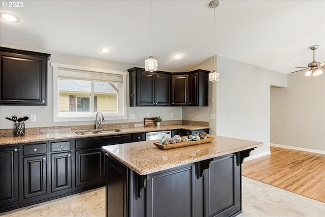 kitchen with a center island, light stone counters, dishwasher, a sink, and decorative light fixtures