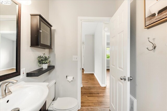 bathroom with visible vents, toilet, wood finished floors, a sink, and baseboards