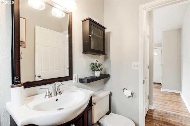 half bath with toilet, vanity, wood finished floors, and baseboards