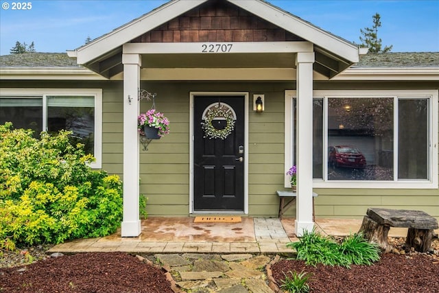 doorway to property with a porch and roof with shingles