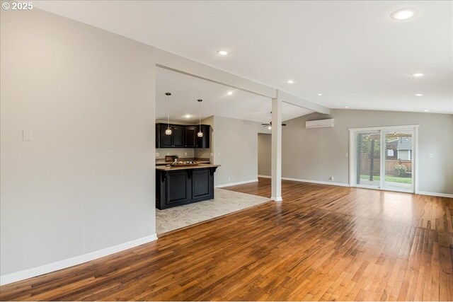 unfurnished living room with a wall mounted air conditioner, hardwood / wood-style flooring, baseboards, and lofted ceiling