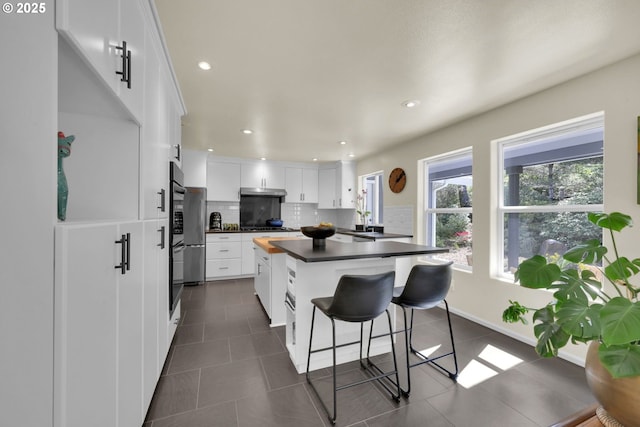 88005 Windleaf Way, Florence, OR 97439 - kitchen with dark countertops, dark tile patterned flooring, white cabinets, a breakfast bar area, and backsplash