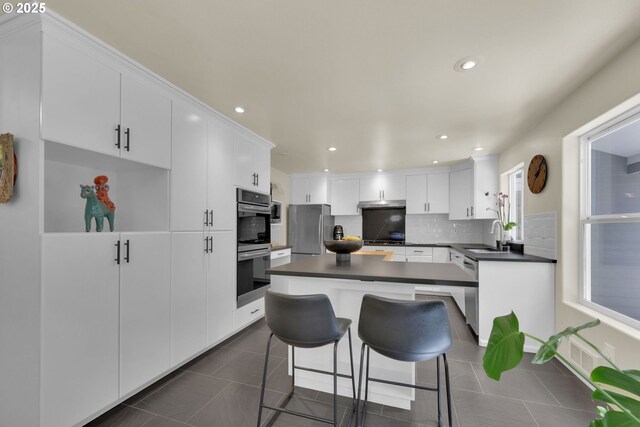 88005 Windleaf Way, Florence, OR 97439 - kitchen with dark countertops, tasteful backsplash, white cabinetry, appliances with stainless steel finishes, and a kitchen island