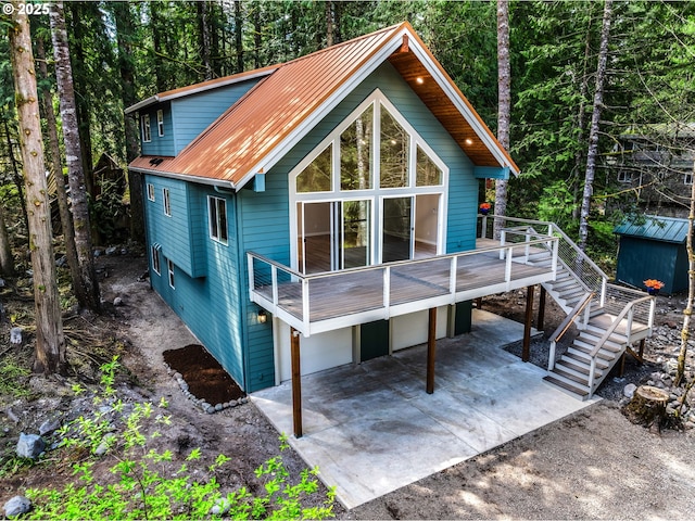 exterior space featuring metal roof, a wooden deck, a patio area, stairway, and a forest view
