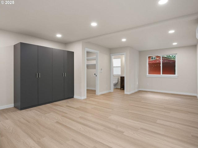 unfurnished bedroom featuring recessed lighting, a spacious closet, connected bathroom, baseboards, and light wood-style flooring