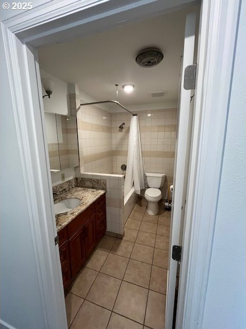 full bath featuring tile patterned floors, toilet, tiled shower / bath combo, tile walls, and vanity