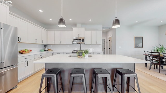 665 Browndell Ln, Stanfield, OR 97875 - kitchen with stainless steel appliances, light wood finished floors, decorative backsplash, a kitchen breakfast bar, and recessed lighting