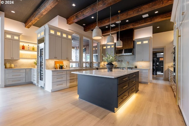 kitchen with beamed ceiling, light hardwood / wood-style flooring, hanging light fixtures, and a kitchen island with sink