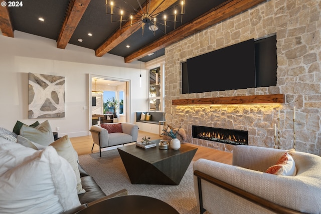 living room featuring an inviting chandelier, beam ceiling, hardwood / wood-style floors, and a stone fireplace