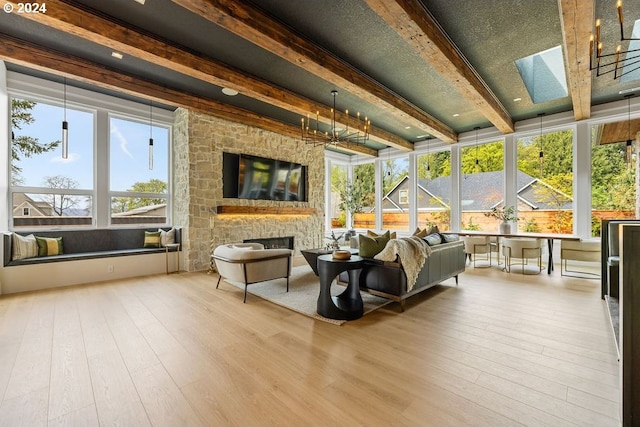 sunroom featuring beam ceiling, an inviting chandelier, a skylight, and a fireplace