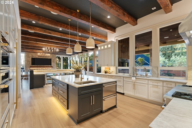 kitchen featuring light stone countertops, white cabinets, beamed ceiling, sink, and a center island with sink