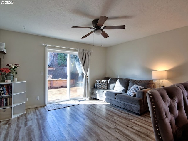 living room featuring ceiling fan, a textured ceiling, baseboards, and wood finished floors