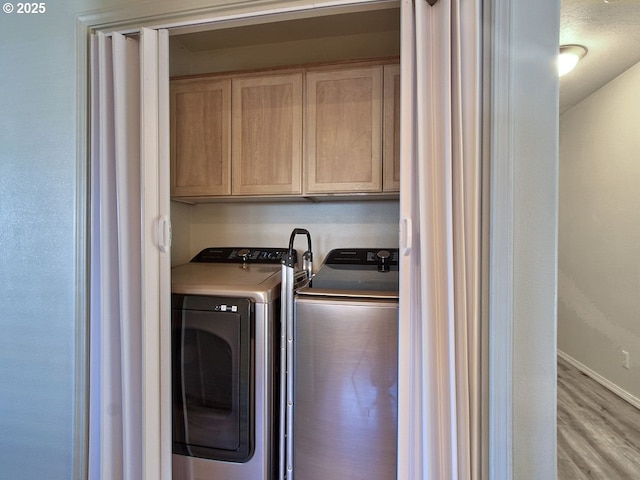 washroom featuring light wood-type flooring, independent washer and dryer, cabinet space, and baseboards