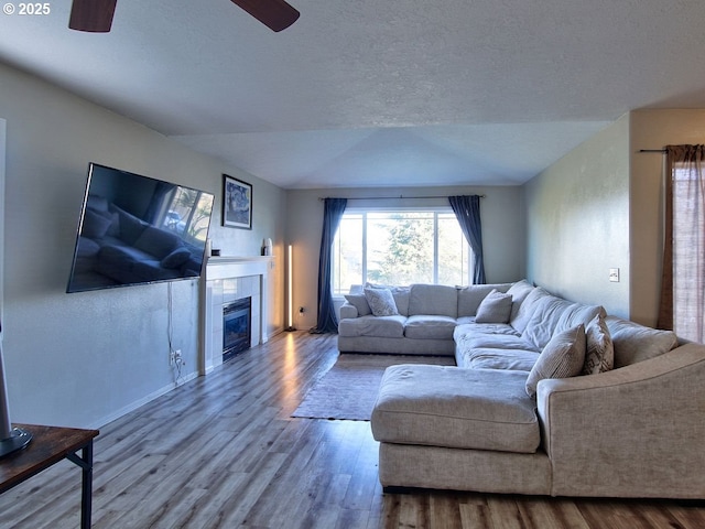 living area with a ceiling fan, a tile fireplace, a textured ceiling, and wood finished floors