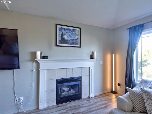 living area with wood finished floors, plenty of natural light, a tile fireplace, and baseboards