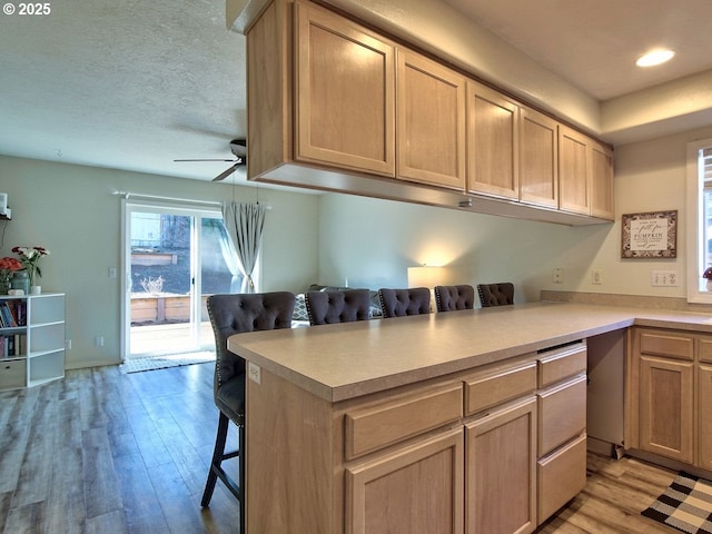 kitchen with a ceiling fan, light countertops, a textured ceiling, light wood-type flooring, and a kitchen bar