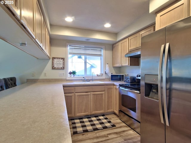 kitchen with light wood-style flooring, under cabinet range hood, stainless steel appliances, a sink, and light countertops