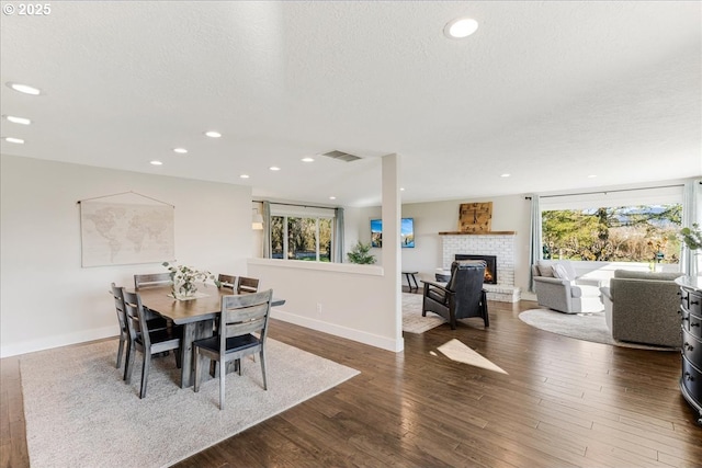 dining area featuring a brick fireplace, wood finished floors, visible vents, and a wealth of natural light