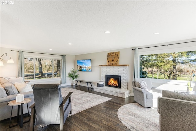 living room with a healthy amount of sunlight, a brick fireplace, a textured ceiling, and dark wood-style flooring