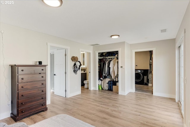 bedroom with light wood finished floors, visible vents, baseboards, washer / dryer, and ensuite bath