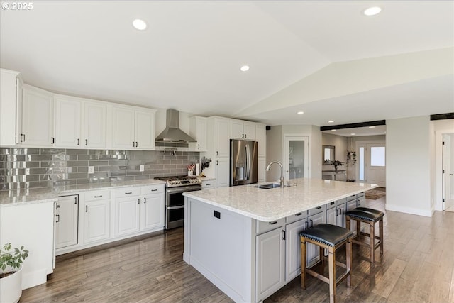 kitchen with white cabinetry, stainless steel appliances, wall chimney range hood, and vaulted ceiling