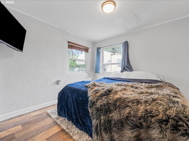 bedroom featuring baseboards, wood finished floors, and a textured wall