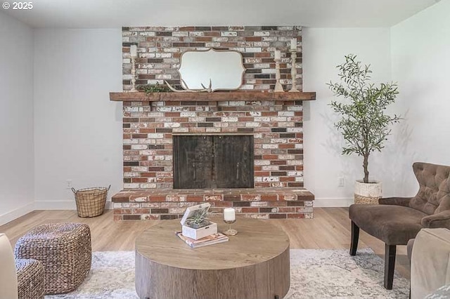 living room featuring a brick fireplace, baseboards, and wood finished floors