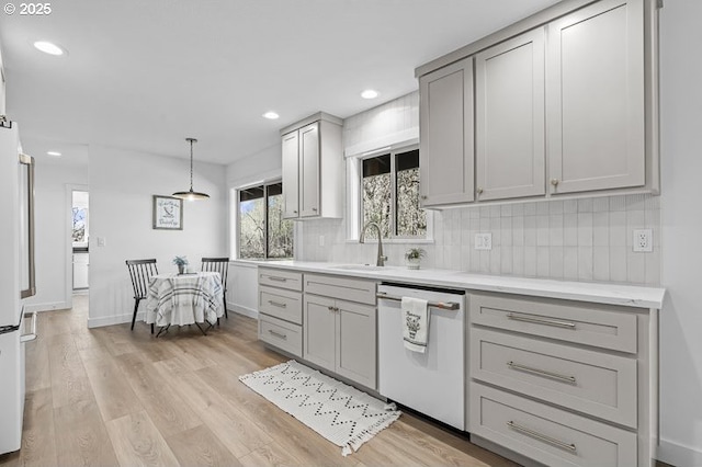 kitchen with light wood-style flooring, a sink, light countertops, dishwasher, and tasteful backsplash