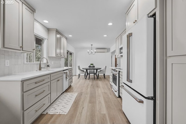 kitchen with tasteful backsplash, gray cabinetry, a wall mounted AC, a sink, and white appliances