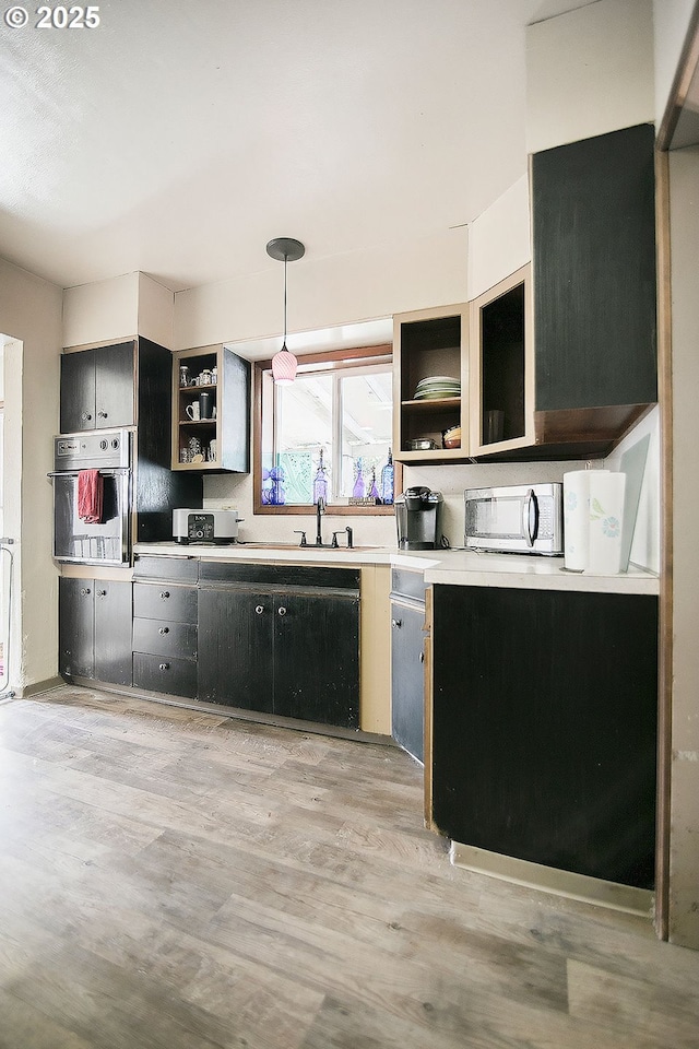 kitchen with light wood-style flooring, open shelves, stainless steel microwave, decorative light fixtures, and oven