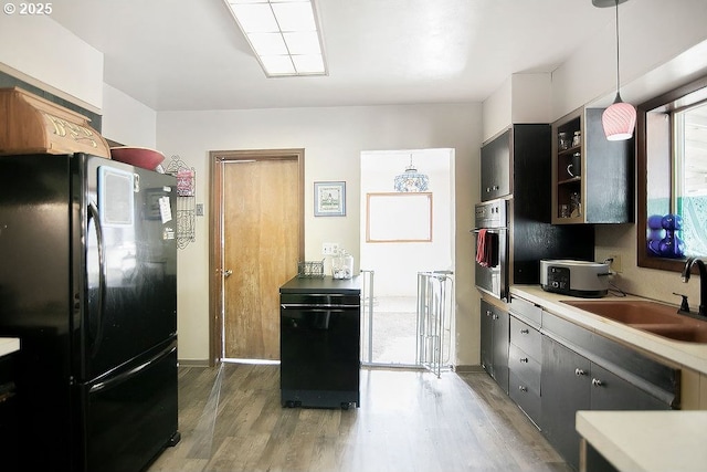 kitchen with light countertops, freestanding refrigerator, light wood finished floors, wall oven, and a sink