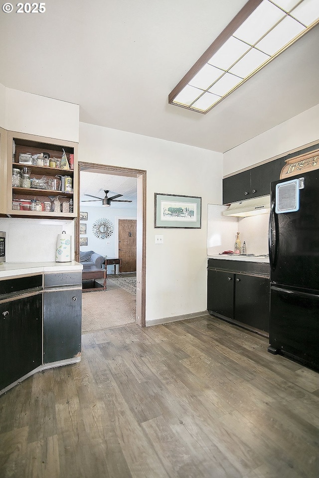 kitchen featuring light countertops, freestanding refrigerator, open shelves, dark cabinetry, and wood finished floors