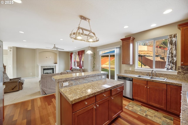 kitchen featuring pendant lighting, sink, dishwasher, a center island, and light stone countertops