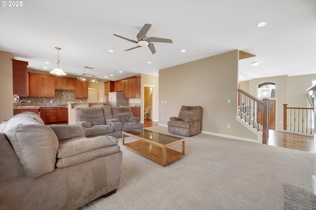 living room featuring ceiling fan with notable chandelier, sink, and light colored carpet