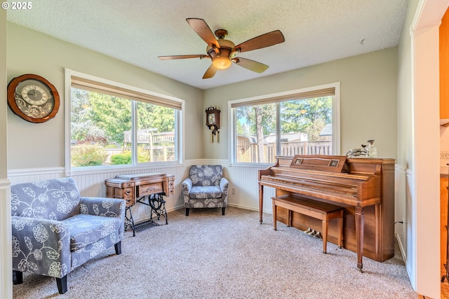 sitting room with a textured ceiling, ceiling fan, wainscoting, and carpet