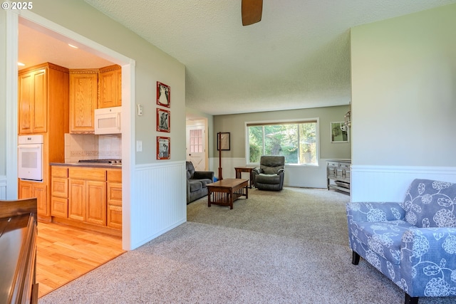 living room featuring a ceiling fan, light carpet, wainscoting, and a textured ceiling