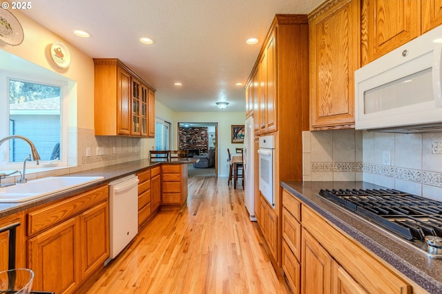 kitchen with dark countertops, white appliances, brown cabinets, a sink, and light wood finished floors