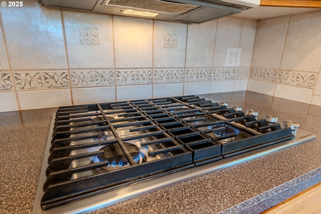 room details with stainless steel gas cooktop, backsplash, exhaust hood, and dark countertops