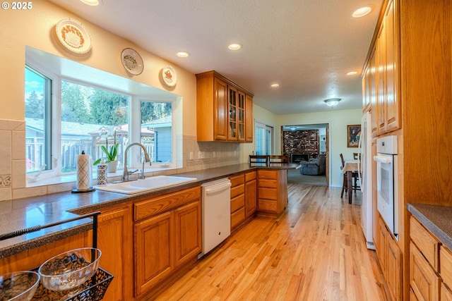 kitchen with dark countertops, brown cabinets, a sink, light wood-style floors, and white appliances
