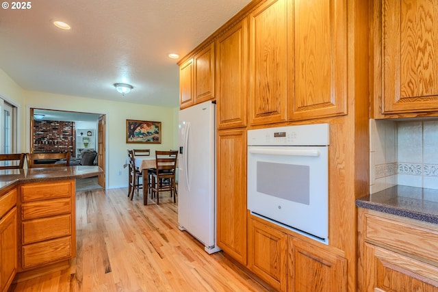 kitchen with light wood-style floors, backsplash, brown cabinets, and white appliances