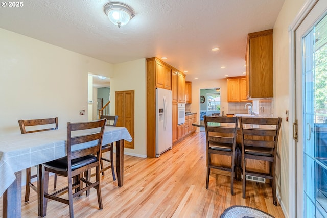 kitchen with a healthy amount of sunlight, brown cabinets, light wood finished floors, and white appliances